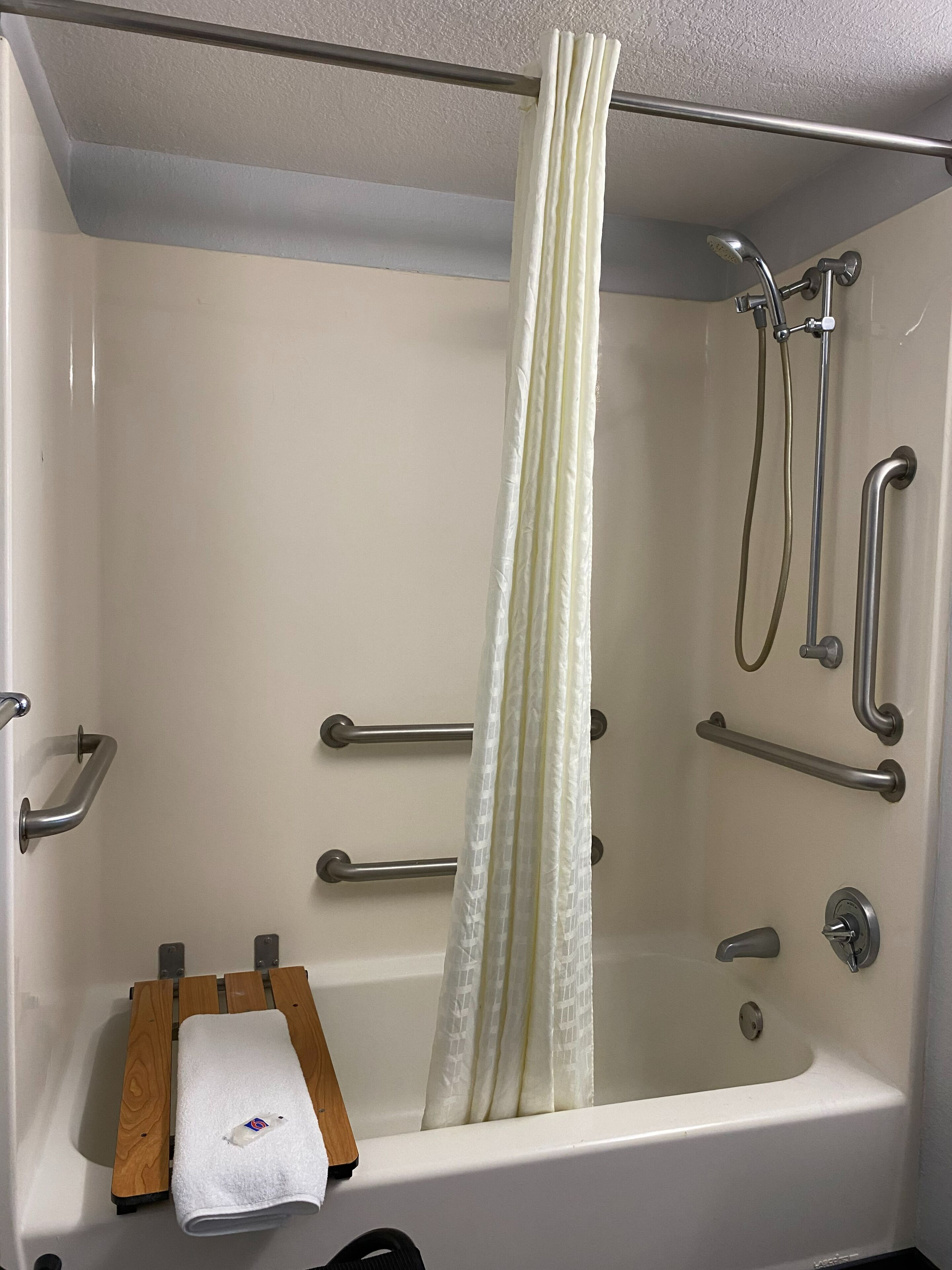 A modern bathroom with a walk-in shower, grab bars, a towel rack, and a wooden bench.