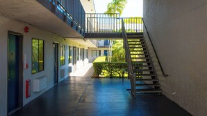 A building with a covered walkway, a staircase, and a view of greenery outside.