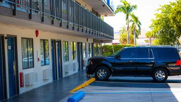 A black SUV parked in front of a building with multiple doors and windows, a balcony, and a palm tree in the background.