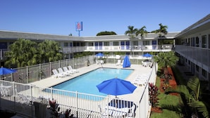 A motel with a swimming pool, lounge chairs, and palm trees. - Motel 6 Lantana, FL (Lantana)