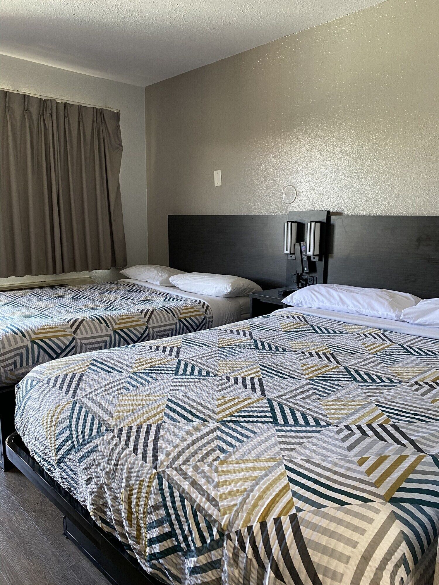 A hotel room with two beds, each with patterned bedding, a dark headboard, and a wall-mounted light fixture.