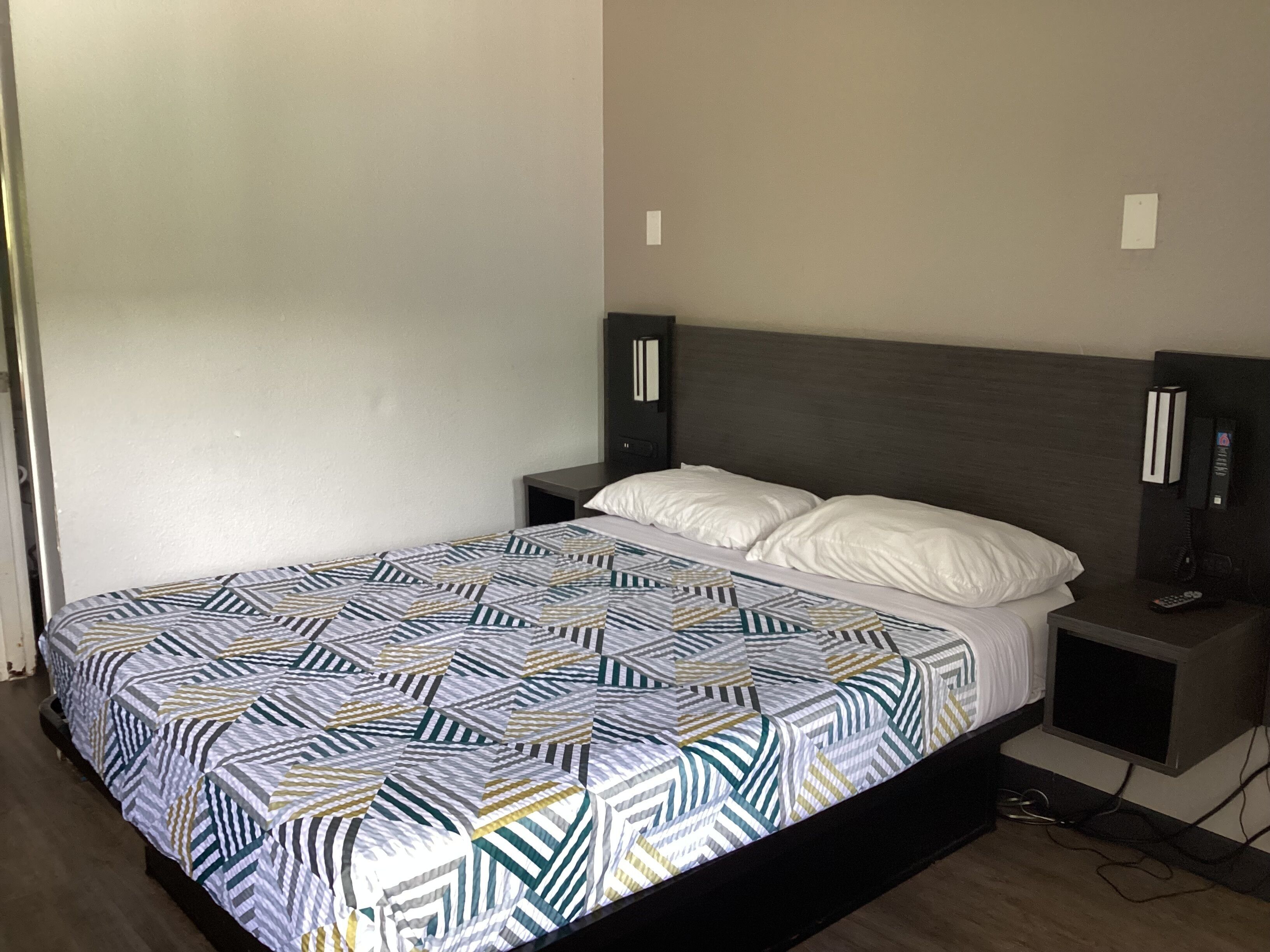 A neatly made bed with a patterned bedspread, a bedside table with a phone, and a wall-mounted light fixture.