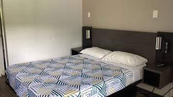 A neatly made bed with a patterned bedspread, a bedside table with a phone, and a wall-mounted light fixture.