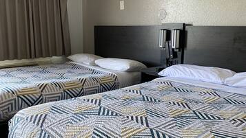 Habitación de hotel con dos camas, cada una con ropa de cama estampada, cabeceros oscuros y una ventana con cortinas.