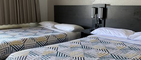 A hotel room with two beds, each with patterned bedding, a dark headboard, and a window with curtains.