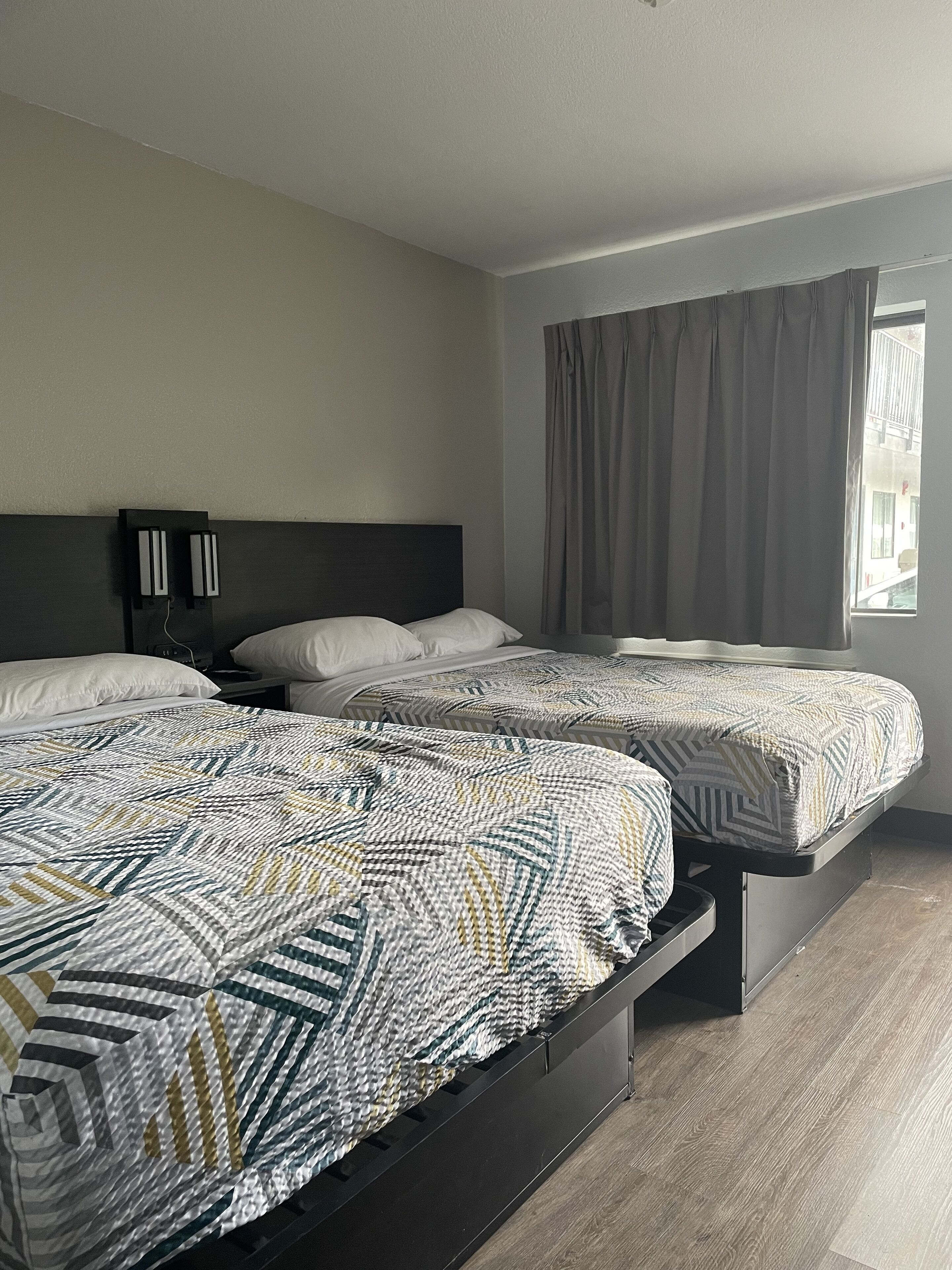 Habitación de hotel con dos camas, cabecera oscura y ventana con cortinas.