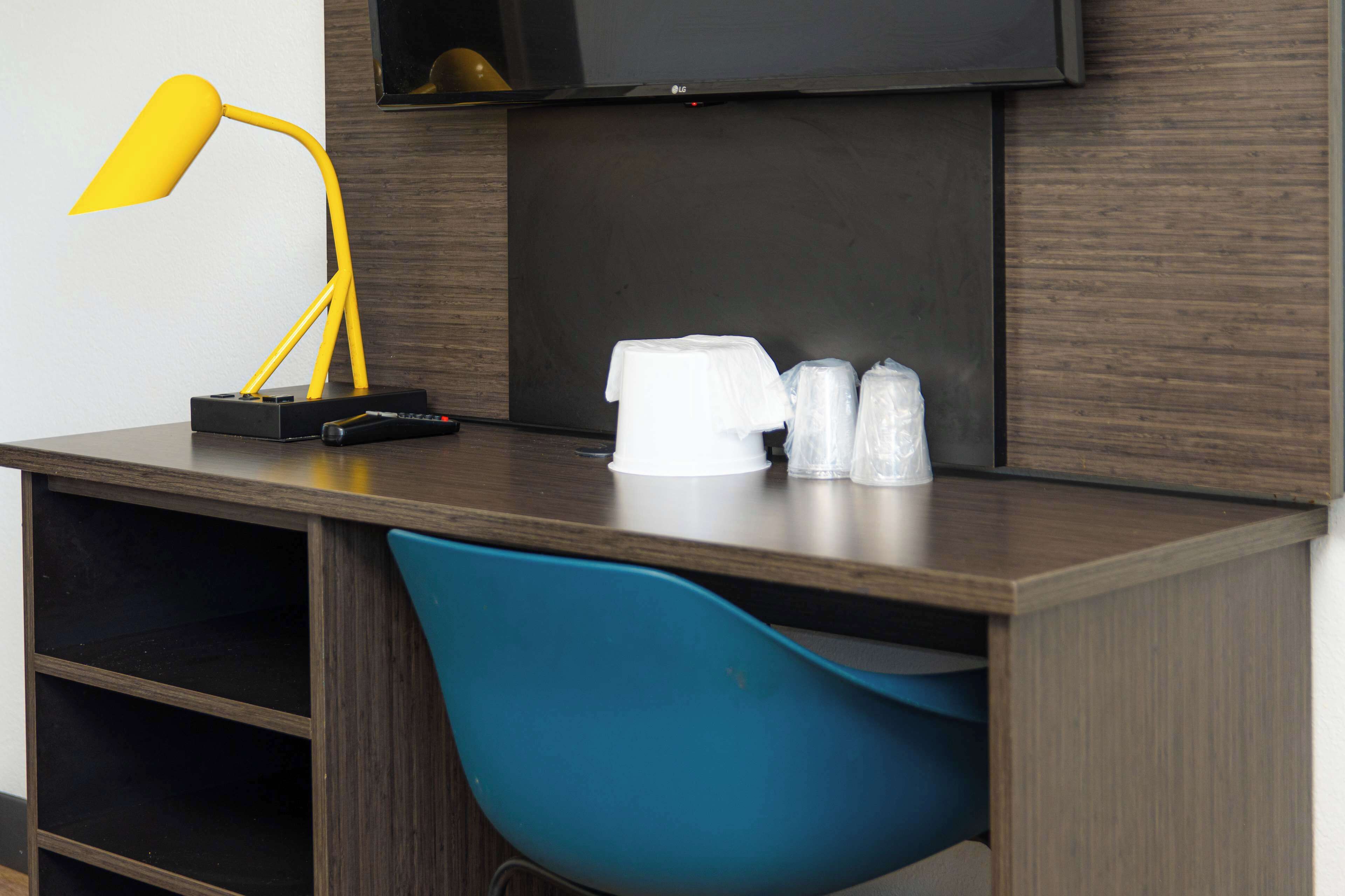 A modern desk with a yellow lamp, a remote control, and a white coffee maker.