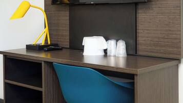 A modern desk with a yellow lamp, a remote control, and a white coffee maker.