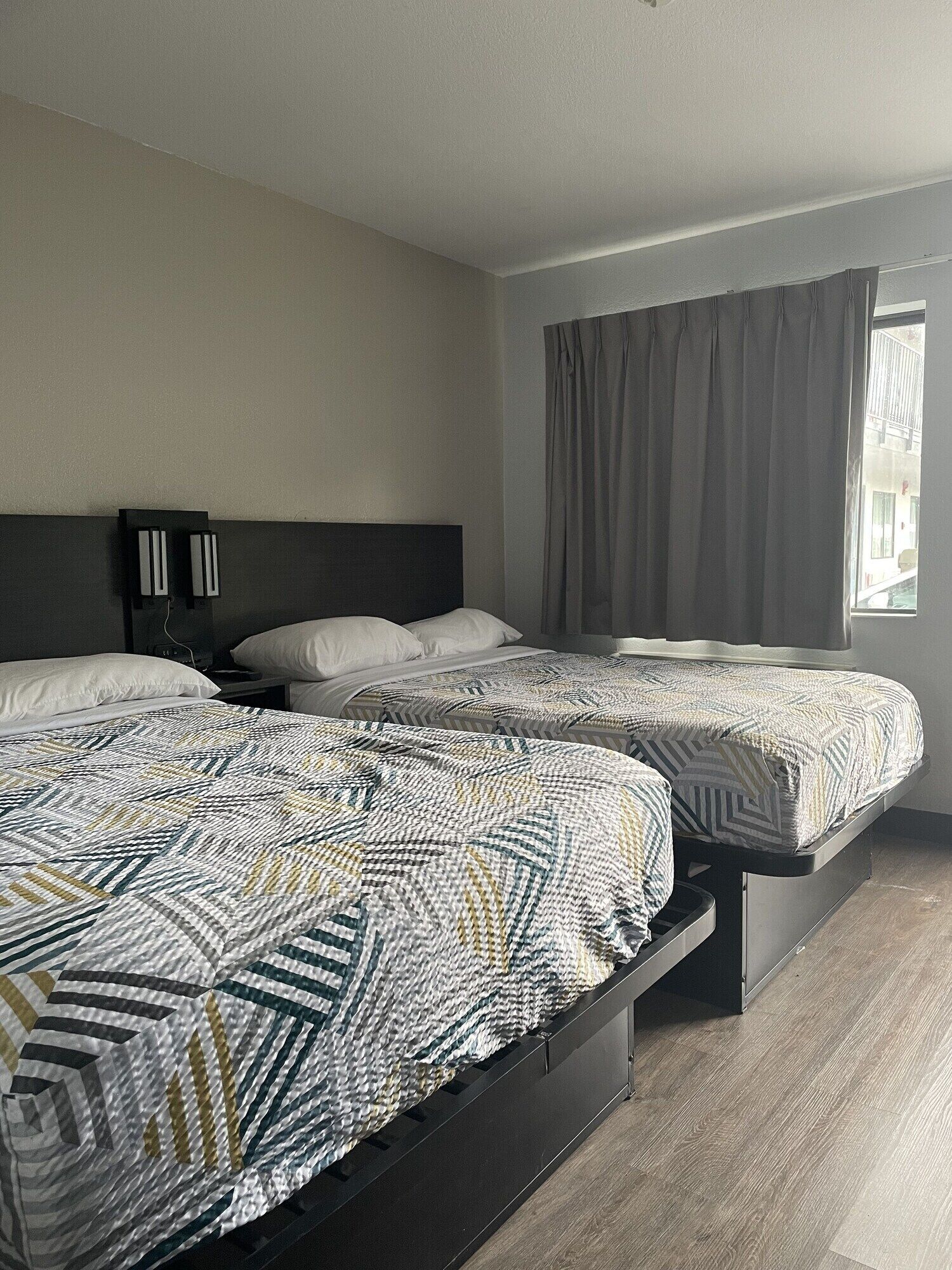 A hotel room with two beds, a dark headboard, and a window with curtains.