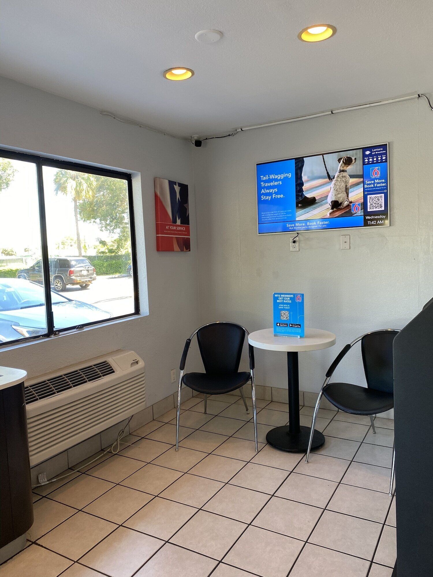 A small, clean room with a window, two chairs, a table, and a poster on the wall.