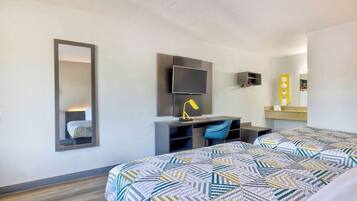 A hotel room with a bed, a desk with a chair, a television, and a mirror.