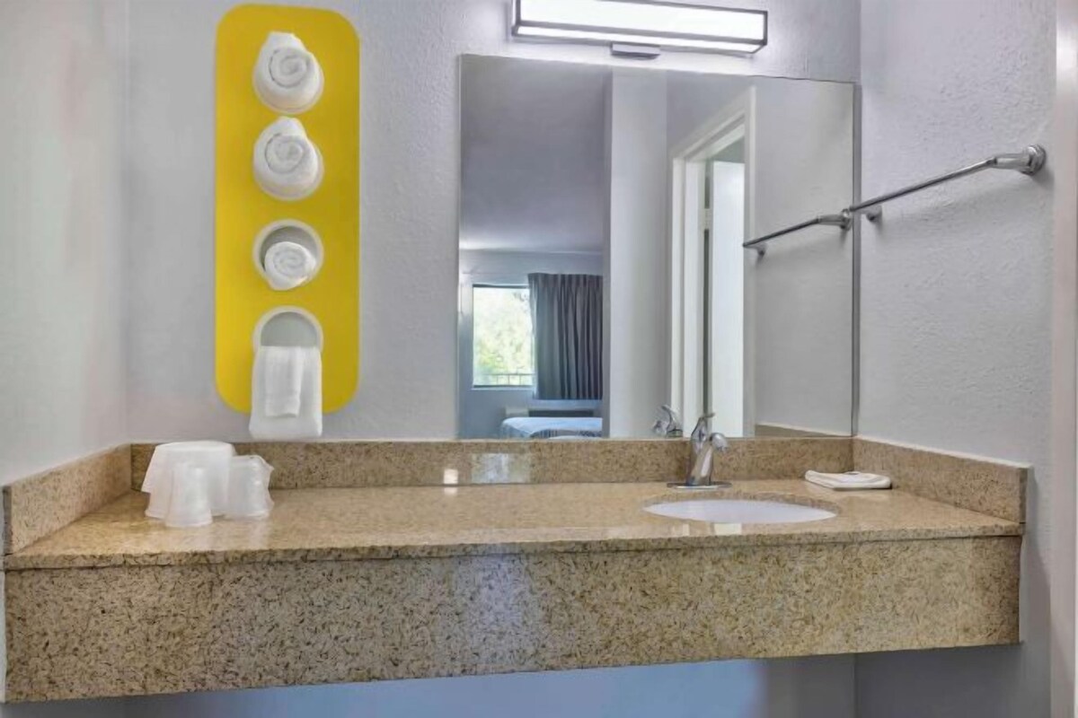A bathroom with a granite countertop, a sink, a mirror, and a towel dispenser.