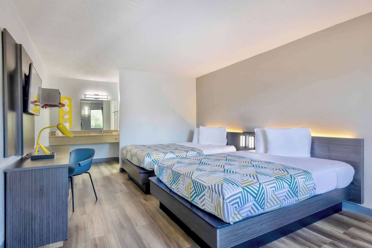 A modern hotel room with a large bed, a desk, a chair, and a mirror.
