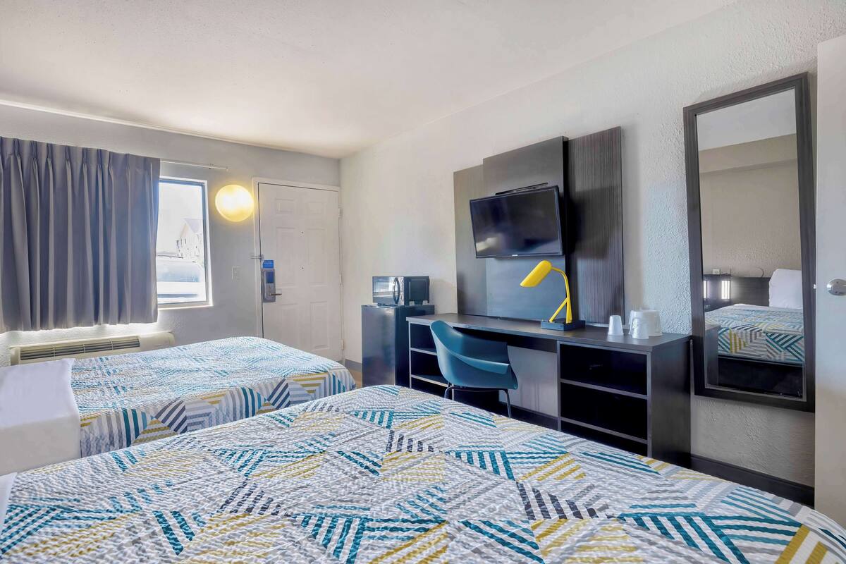A hotel room with two beds, a desk with a chair, a TV, and a large mirror.