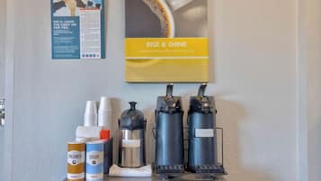 A coffee station with three coffee makers, creamer, sugar, and disposable cups.