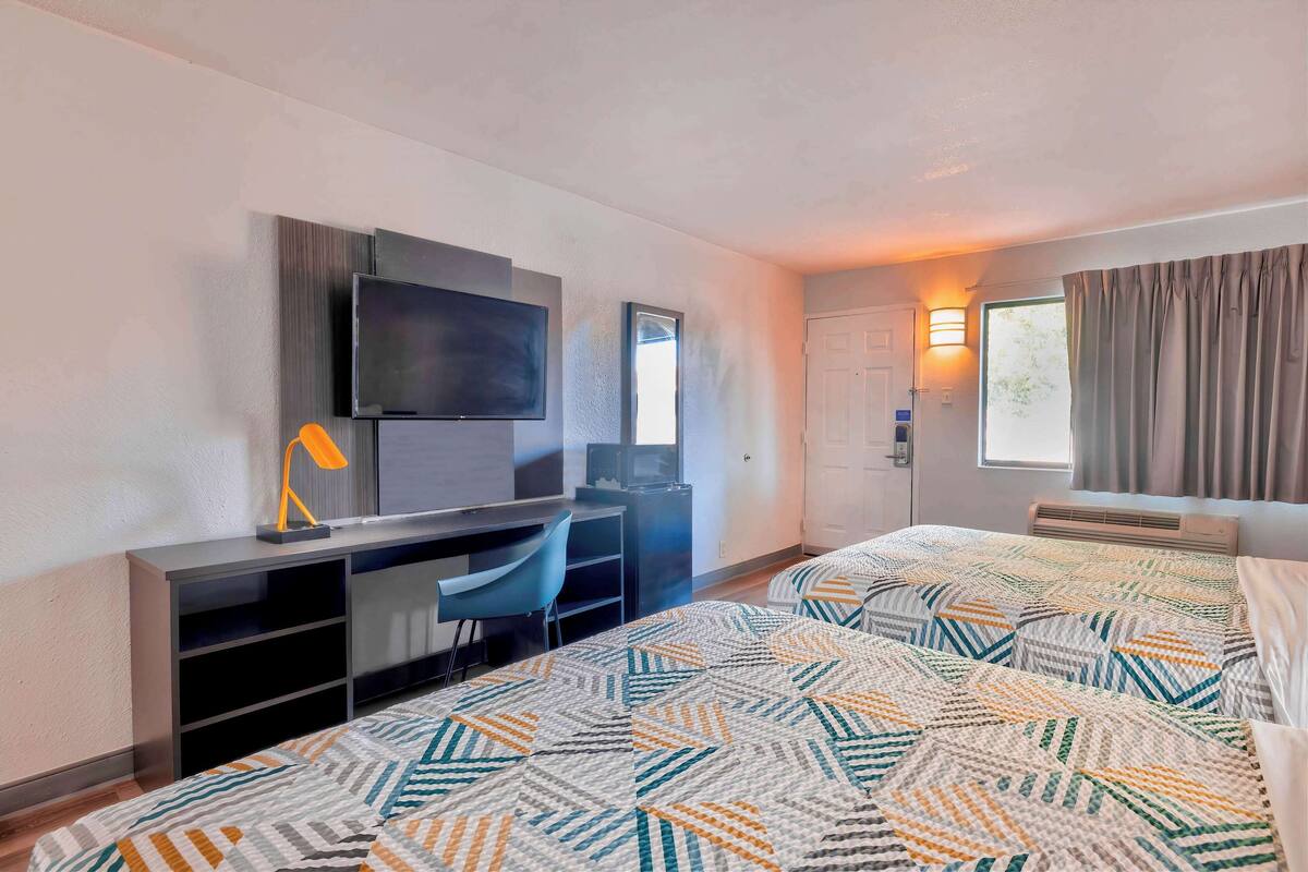 A hotel room with a bed, a desk with a chair, a TV, and a window with curtains.