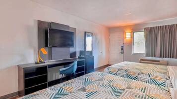 A hotel room with a bed, a desk with a chair, a TV, and a window with curtains.
