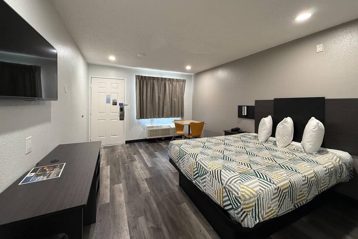 A modern hotel room with a large bed, a desk, a chair, a television, and a window with curtains.