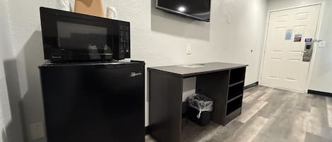 A compact kitchenette with a microwave, refrigerator, and a small desk.