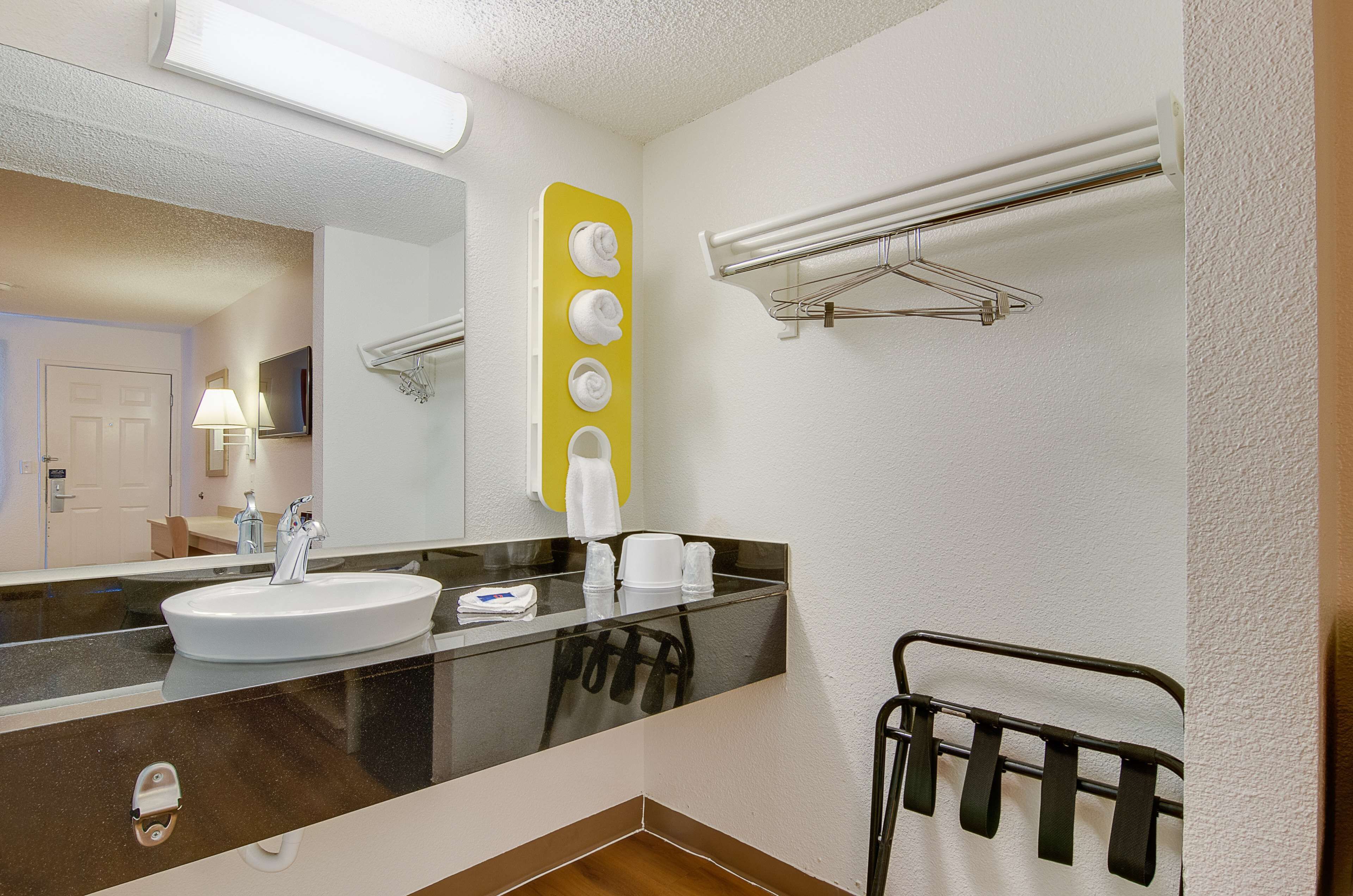 A bathroom with a sink, mirror, towel rack, and a yellow wall decoration.