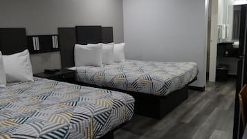 A hotel room with two beds, a small desk, and a bathroom visible through an open door.