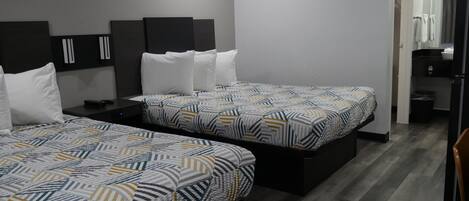 A hotel room with two beds, a small desk, and a bathroom visible through an open door.