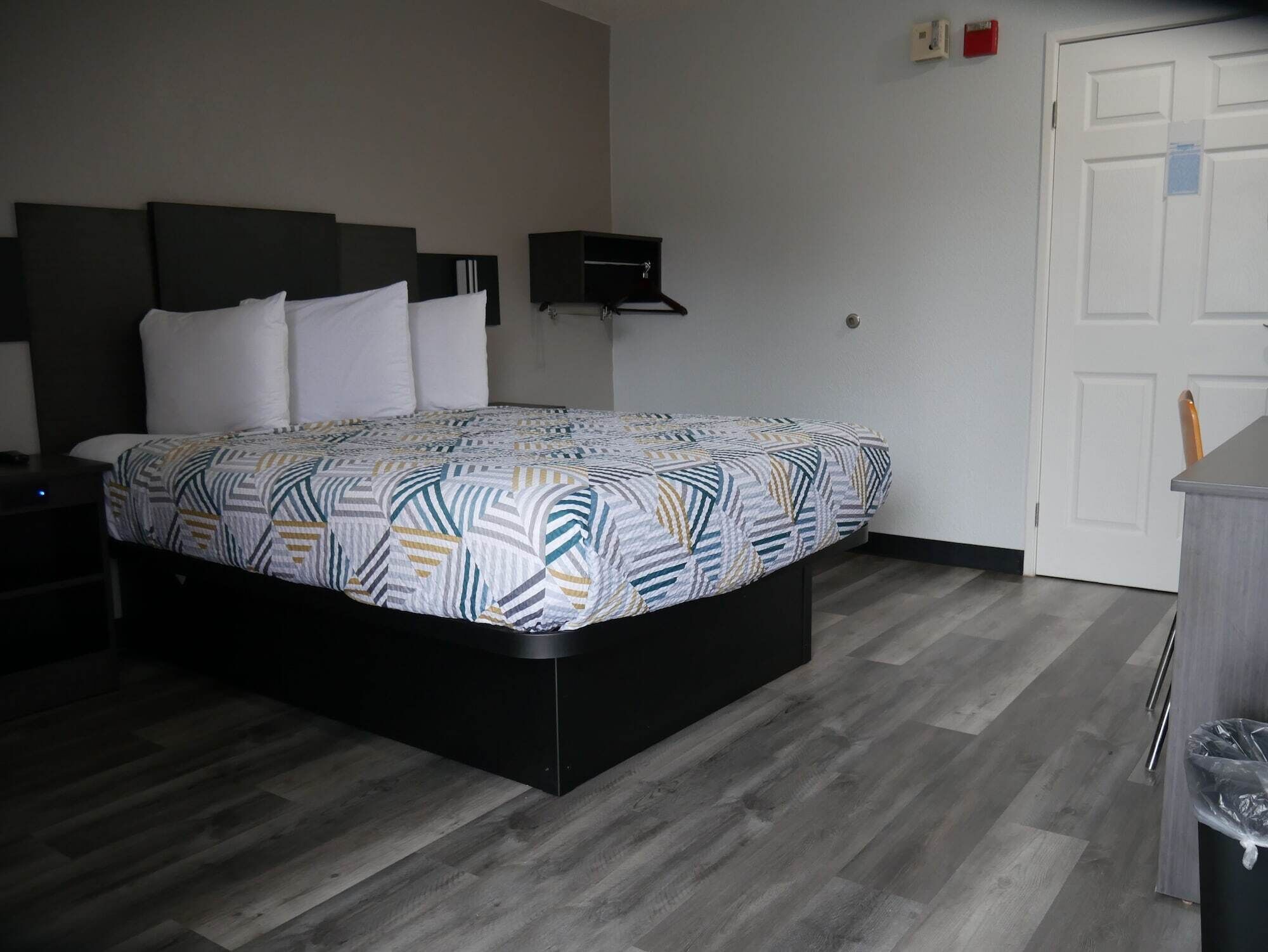 Un dormitorio con una cama, una mesita de noche, un estante en la pared y una puerta.
