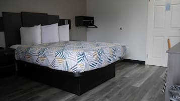 Un dormitorio con una cama, una mesita de noche, un estante en la pared y una puerta.