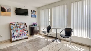 A hotel lobby with a reception desk, a bulletin board with travel brochures, two chairs, a small table, and a TV mounted on the wall. - Motel 6 Tacoma, WA - South (Tacoma)