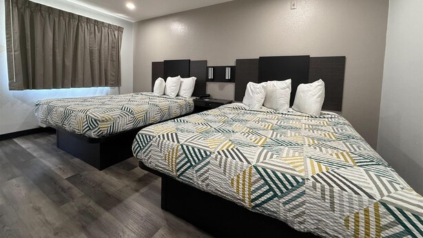 A hotel room with two beds, each with a patterned bedspread, a headboard, and a bedside table. - Motel 6 Tacoma, WA - South (Tacoma)