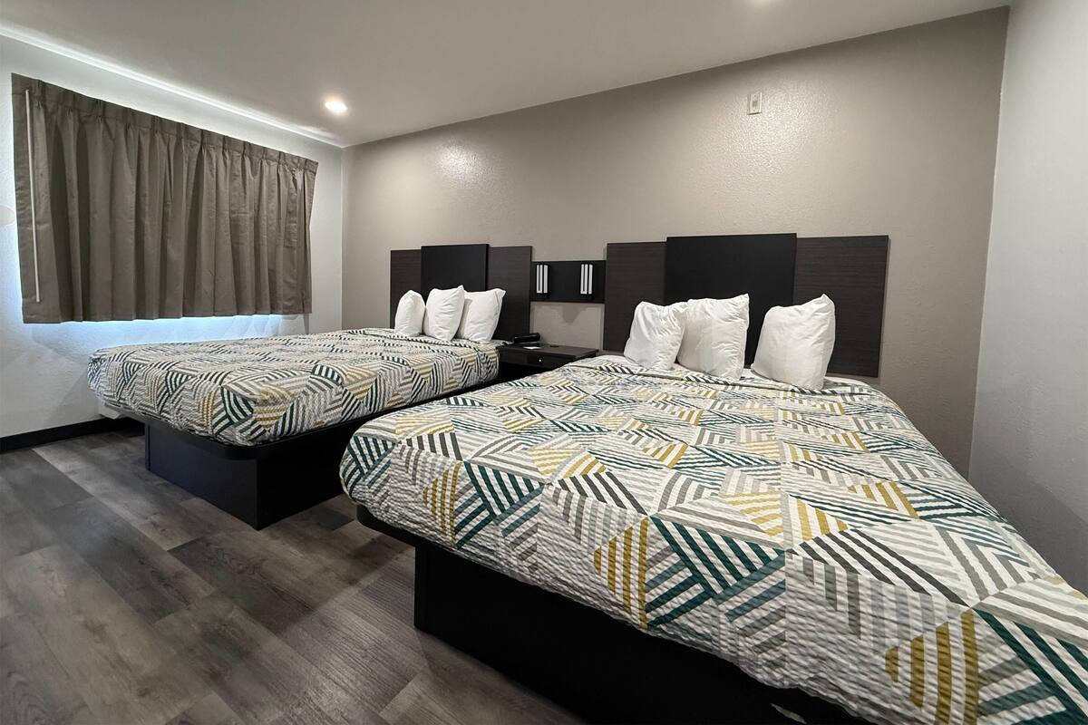 A hotel room with two beds, each with a patterned bedspread, a headboard, and a bedside table.