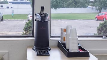 A coffee machine on a counter with disposable cups and a coffee container.