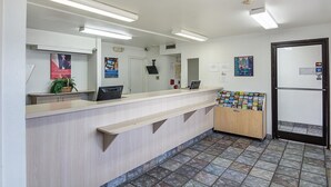 Zona de recepción con mostrador, computadora, planta y puerta con letrero.