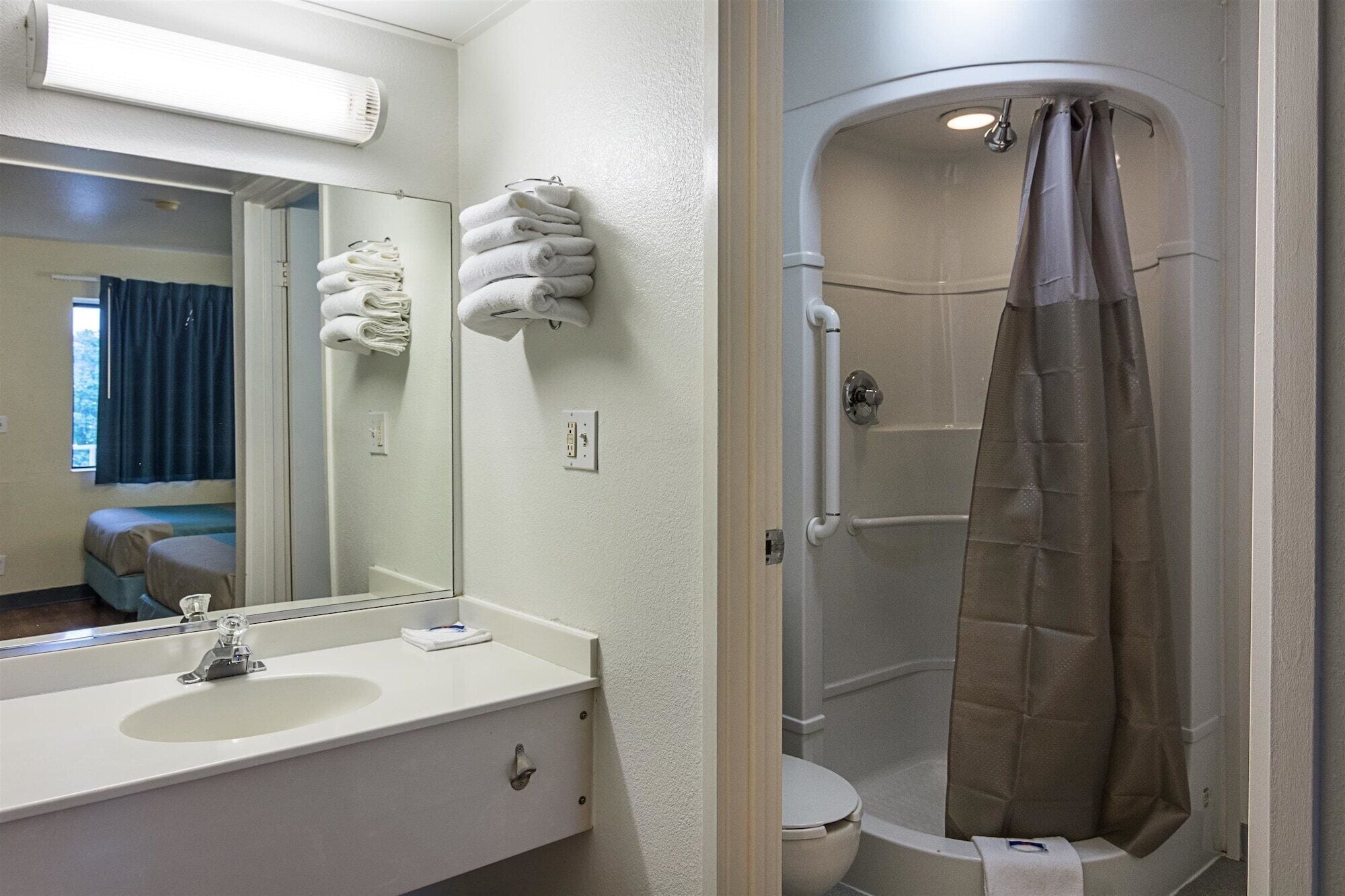A bathroom with a sink, mirror, towel rack, shower curtain, and toilet.