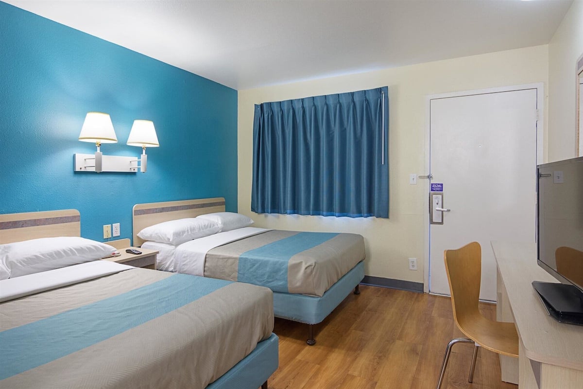Hotellihuone, jossa on kaksi sänkyä, työpöytä, tuoli ja televisio.