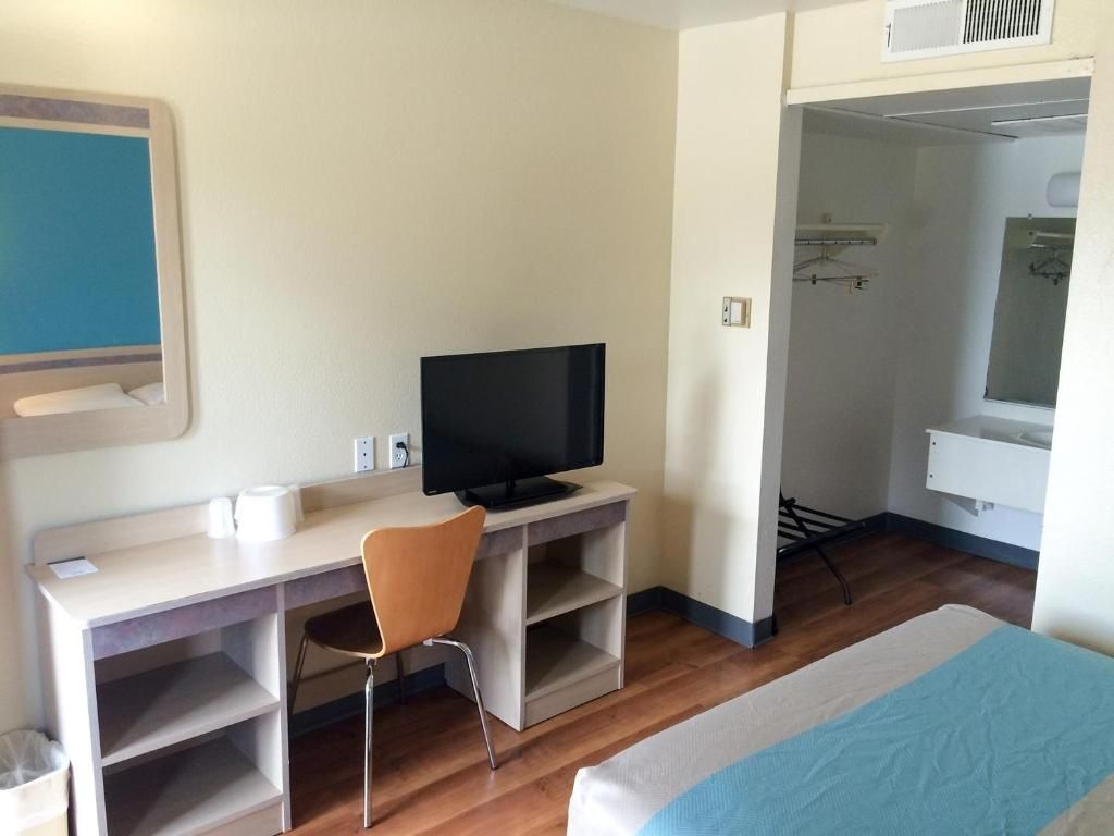 A hotel room with a bed, a desk with a chair, a television, a wardrobe, and a bathroom visible through an open door.