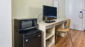 Una kitchenette equipada con microondas, refrigerador y un pequeño escritorio con monitor de computadora y silla.