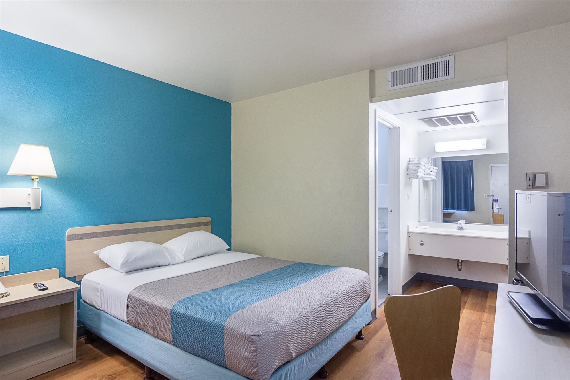 Une chambre d’hôtel équipée d’un lit, d’un bureau, d’une chaise, d’une lampe, d’un miroir et d’un téléviseur.