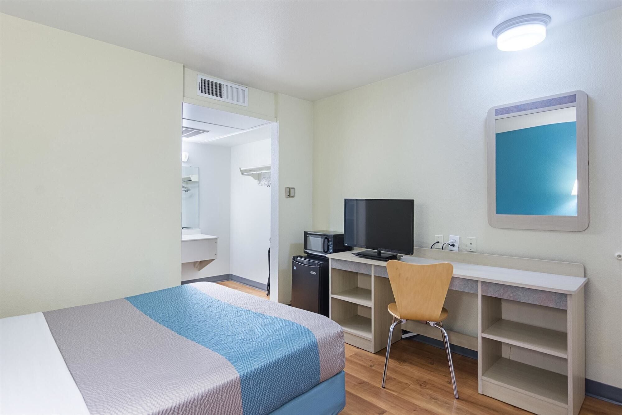 A hotel room with a bed, a desk with a computer, a chair, and a mirror.