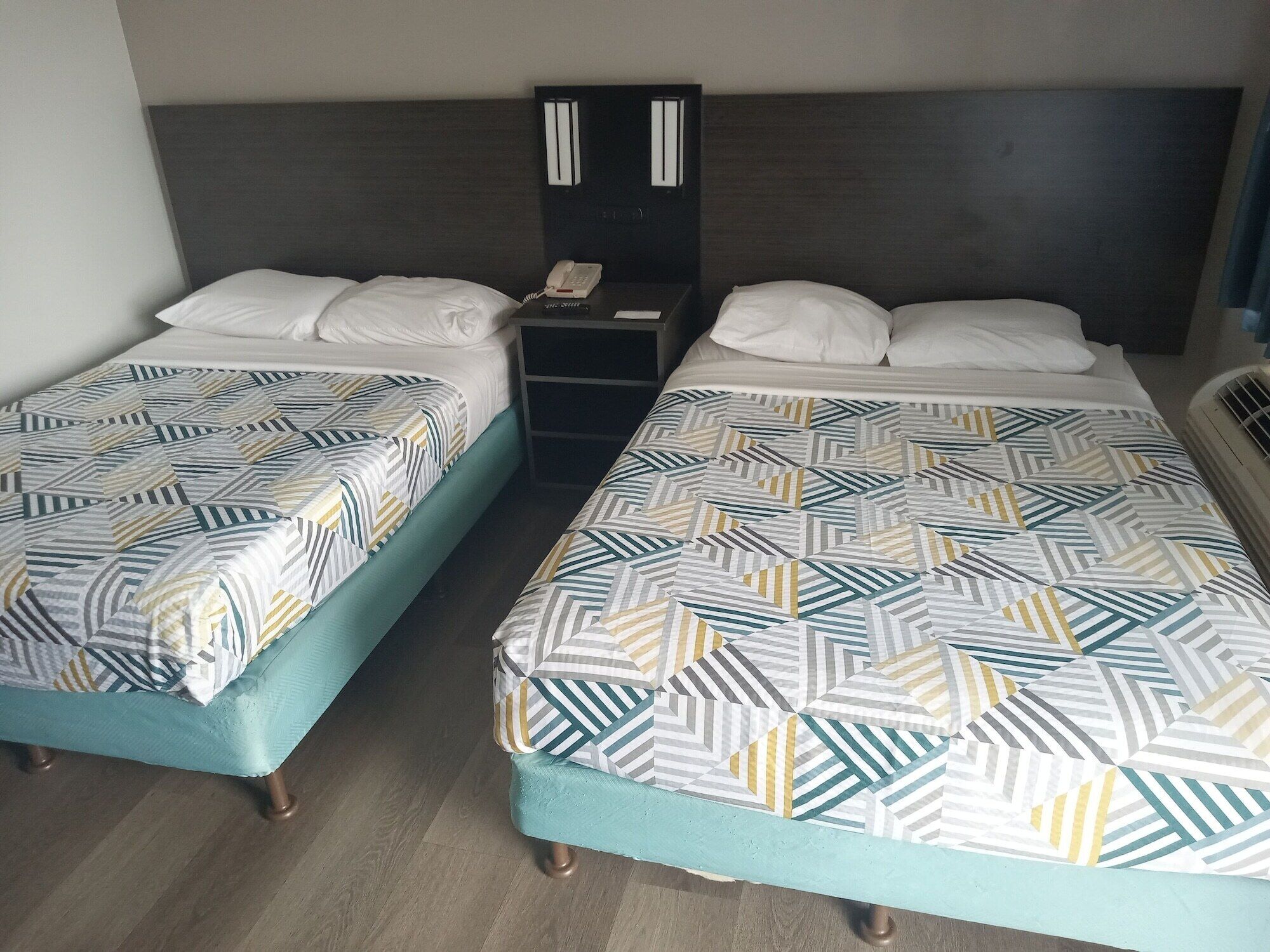 Two single beds with patterned bedding, a bedside table with a phone, and a dark headboard.