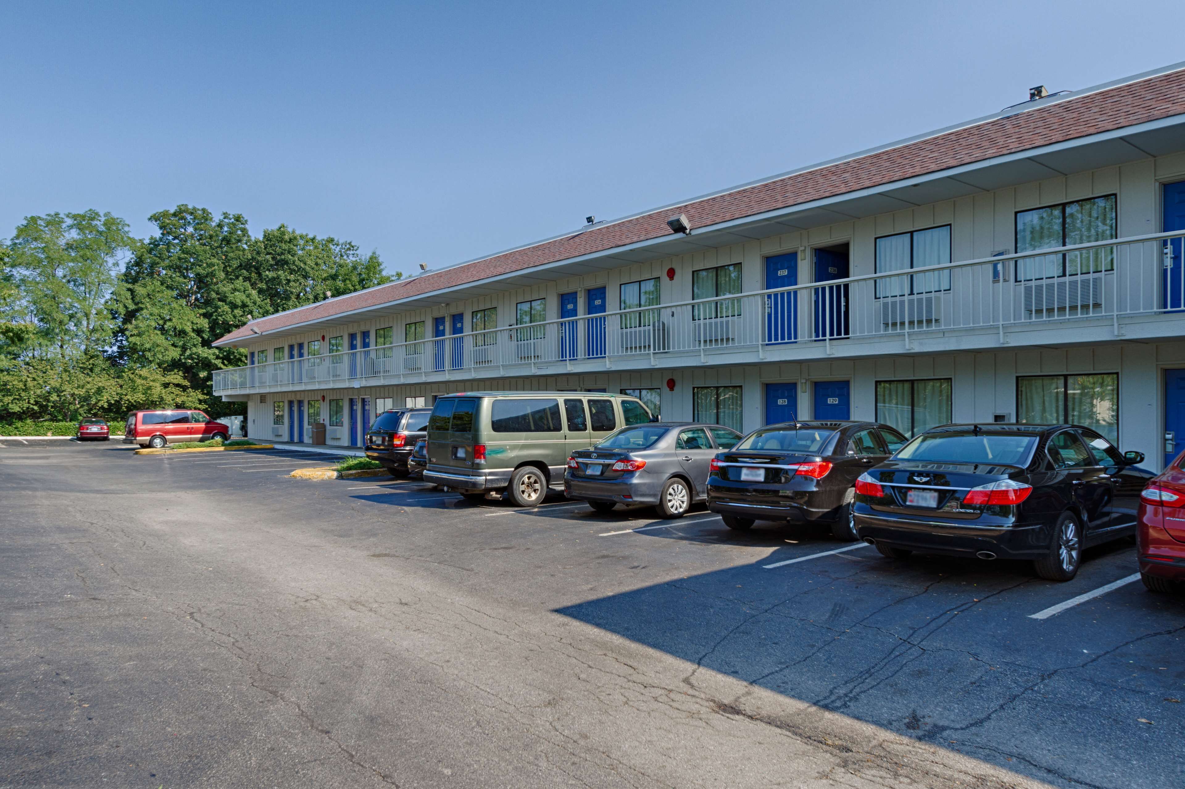 A motel with multiple floors, a parking lot with several cars, and a building with a red roof.