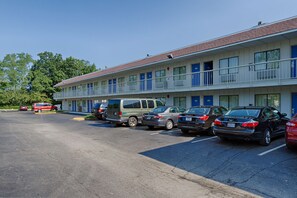 A motel with multiple floors, a parking lot with several cars, and a building with a red roof. - Motel 6 Laurel, DC - Washington Northeast (Laurel)