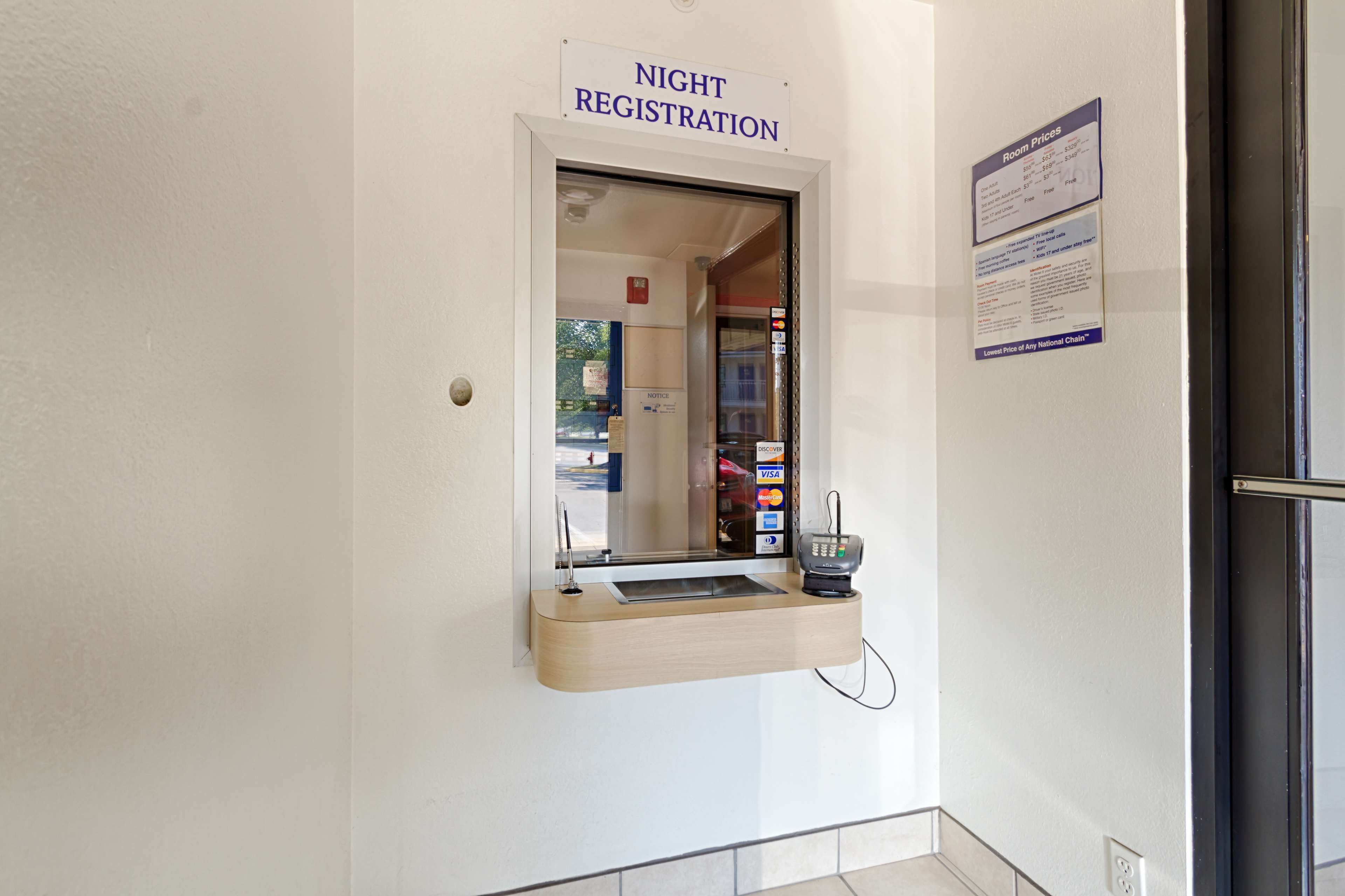 Un comptoir d’enregistrement ouvert la nuit, avec une enseigne au-dessus, un terminal de paiement et un panneau d’affichage.