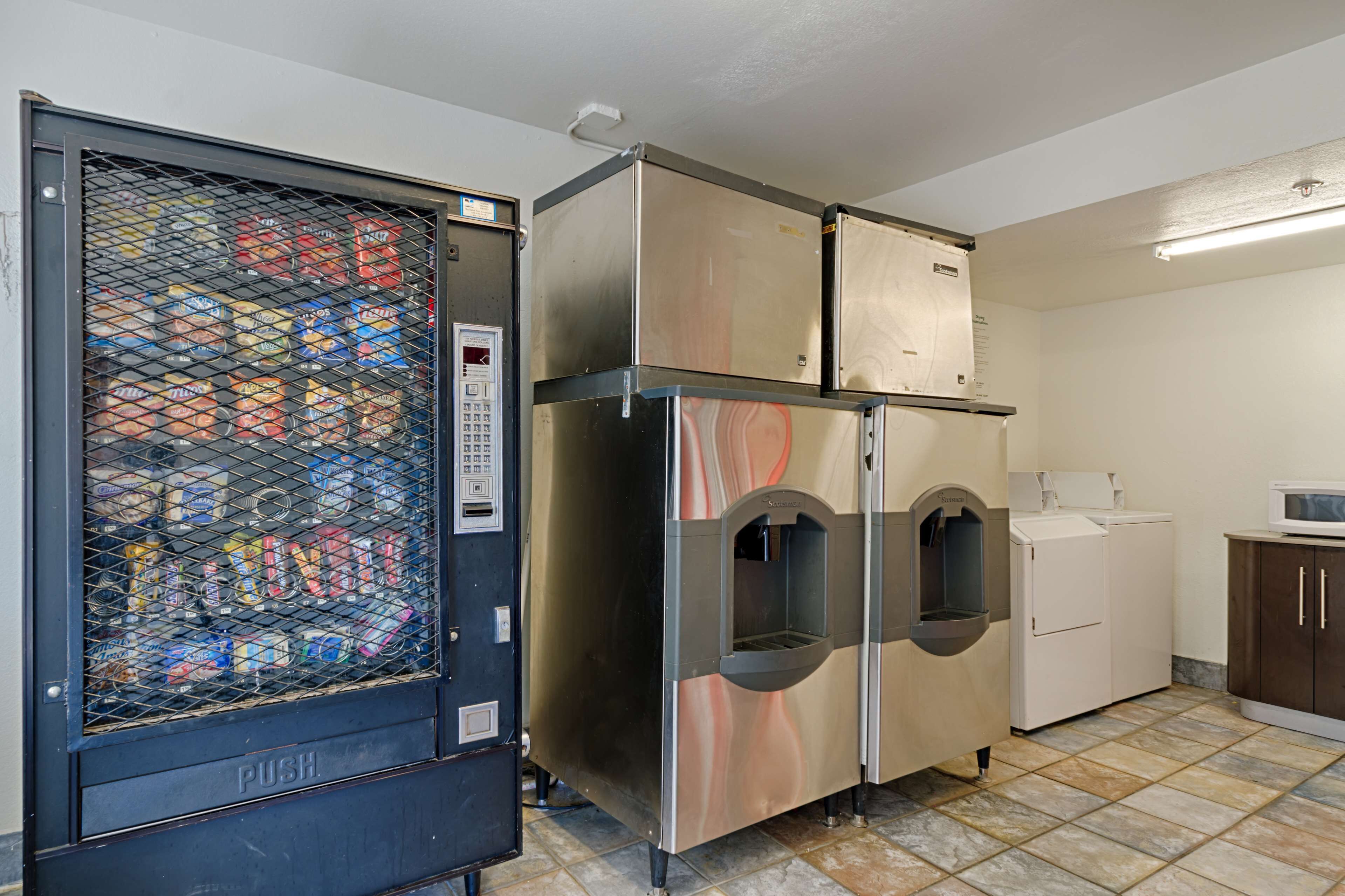 A laundry room with a push cart, a large stainless steel washer and dryer, and a microwave on a cabinet.