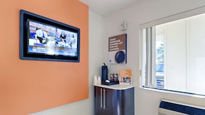 Un espace d’accueil d’hôtel avec un téléviseur diffusant un programme d’information, une machine à café et un panneau indiquant les tarifs applicables le matin.