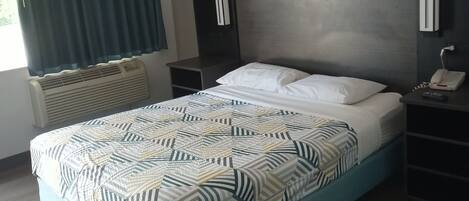 A modern hotel room with a bed, a bedside table with a phone, a nightstand, a wall-mounted lamp, and a window with curtains.