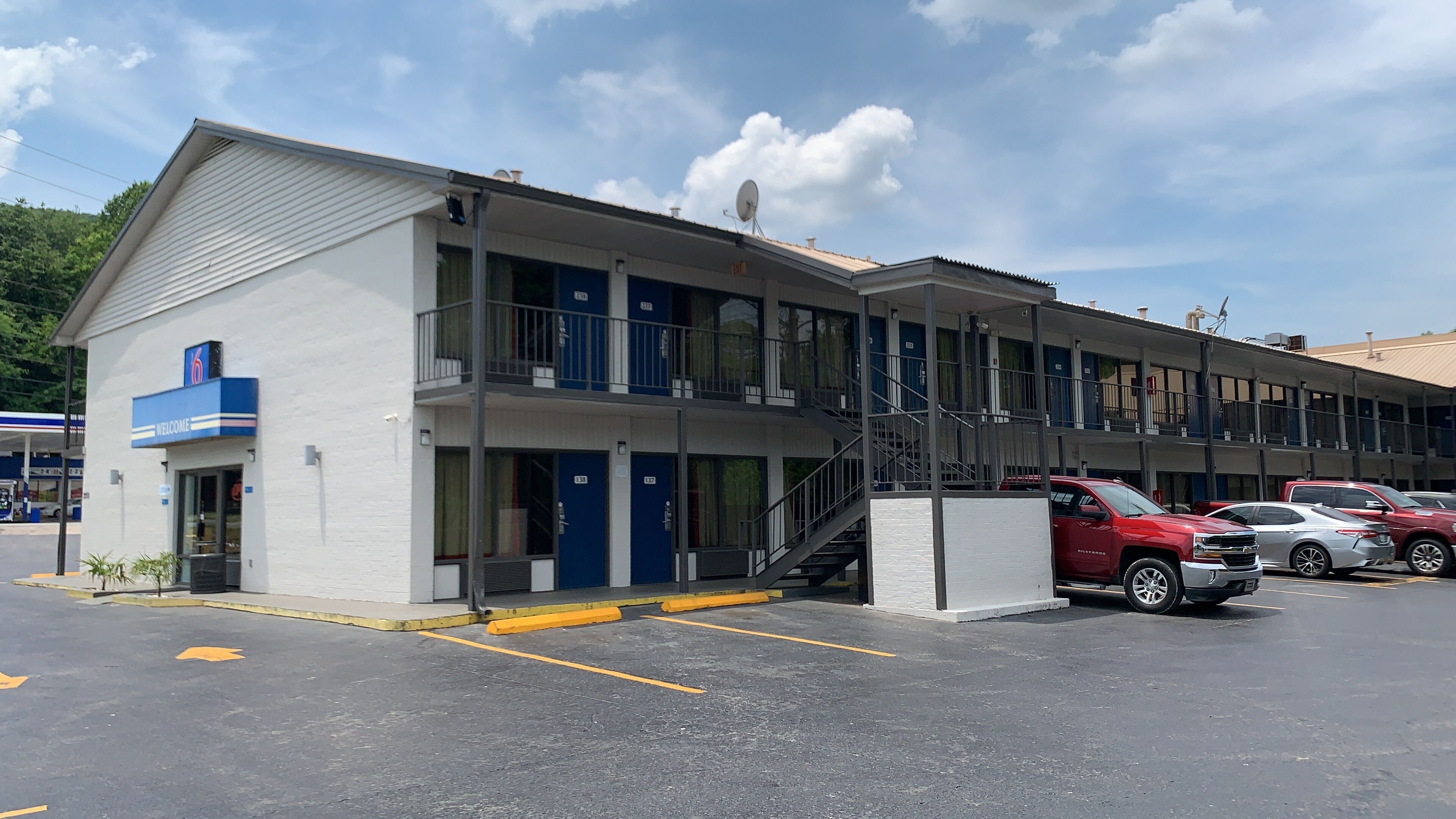 Un motel composé d’un bâtiment à deux étages, de nombreuses chambres et d’un parking où sont stationnées plusieurs voitures.