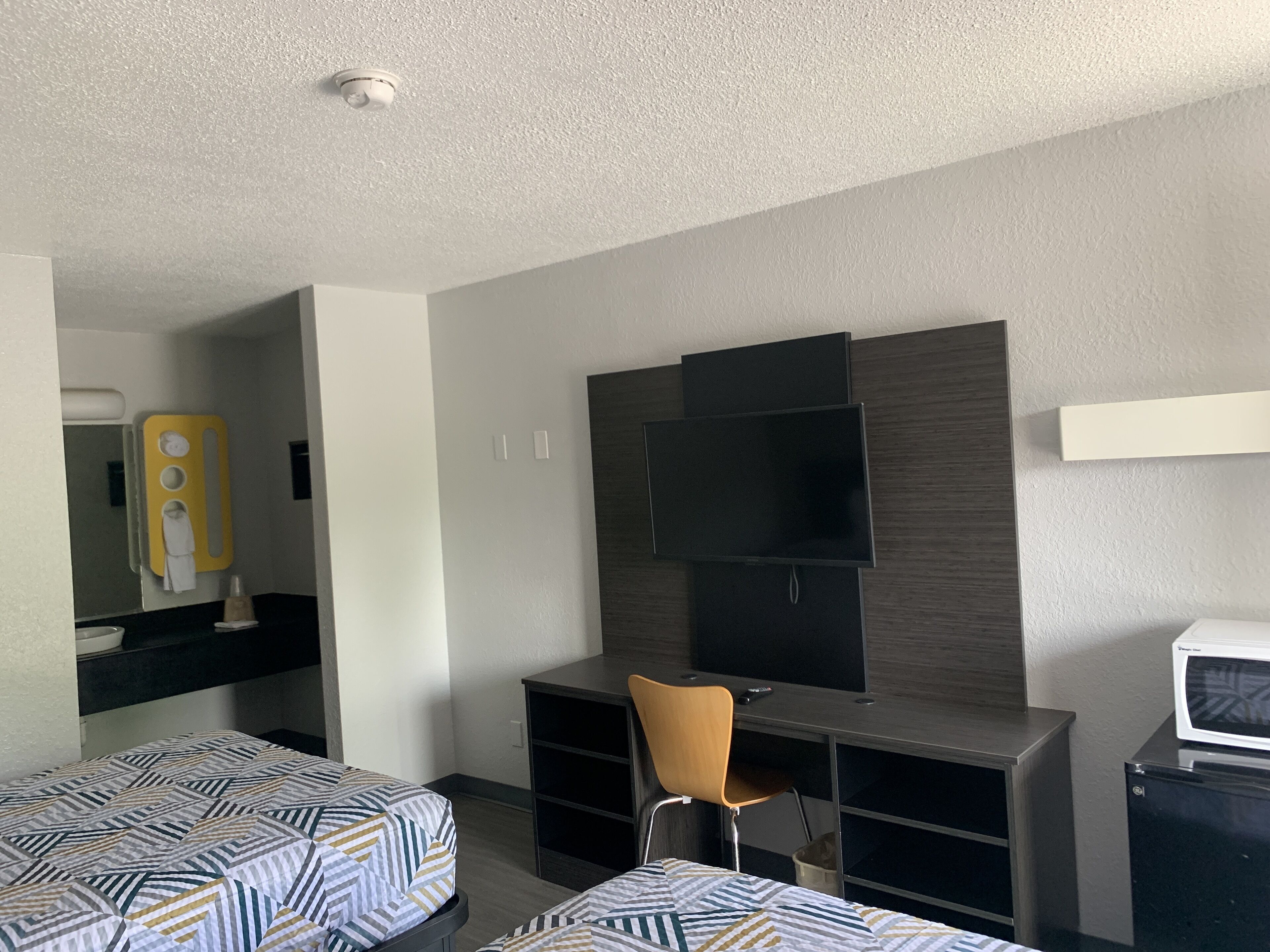 Een hotelkamer met twee bedden, een bureau, een stoel, een televisie en een magnetron.