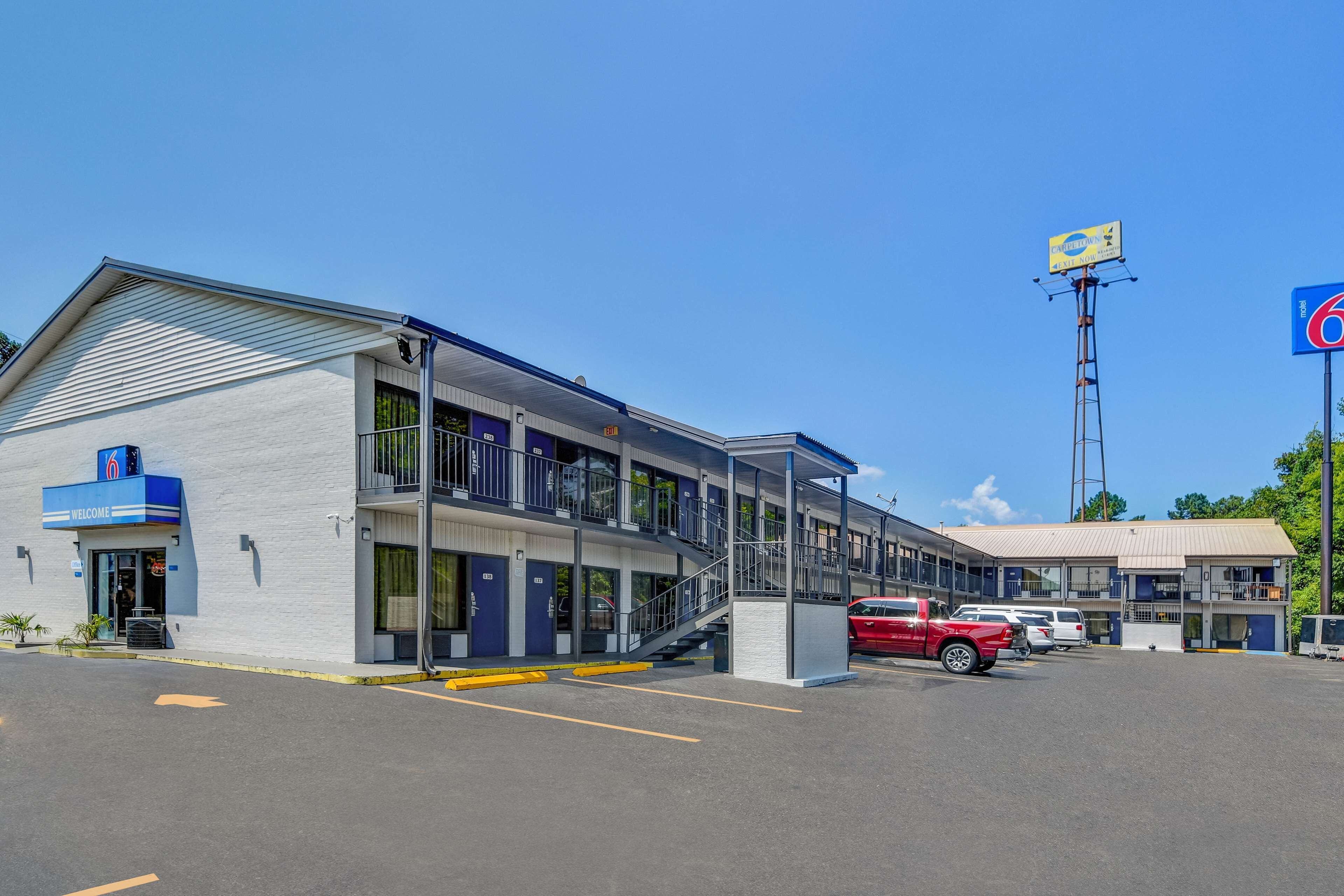 A motel with a '6' sign, a 'Welcome' sign, and a parking lot with several cars.