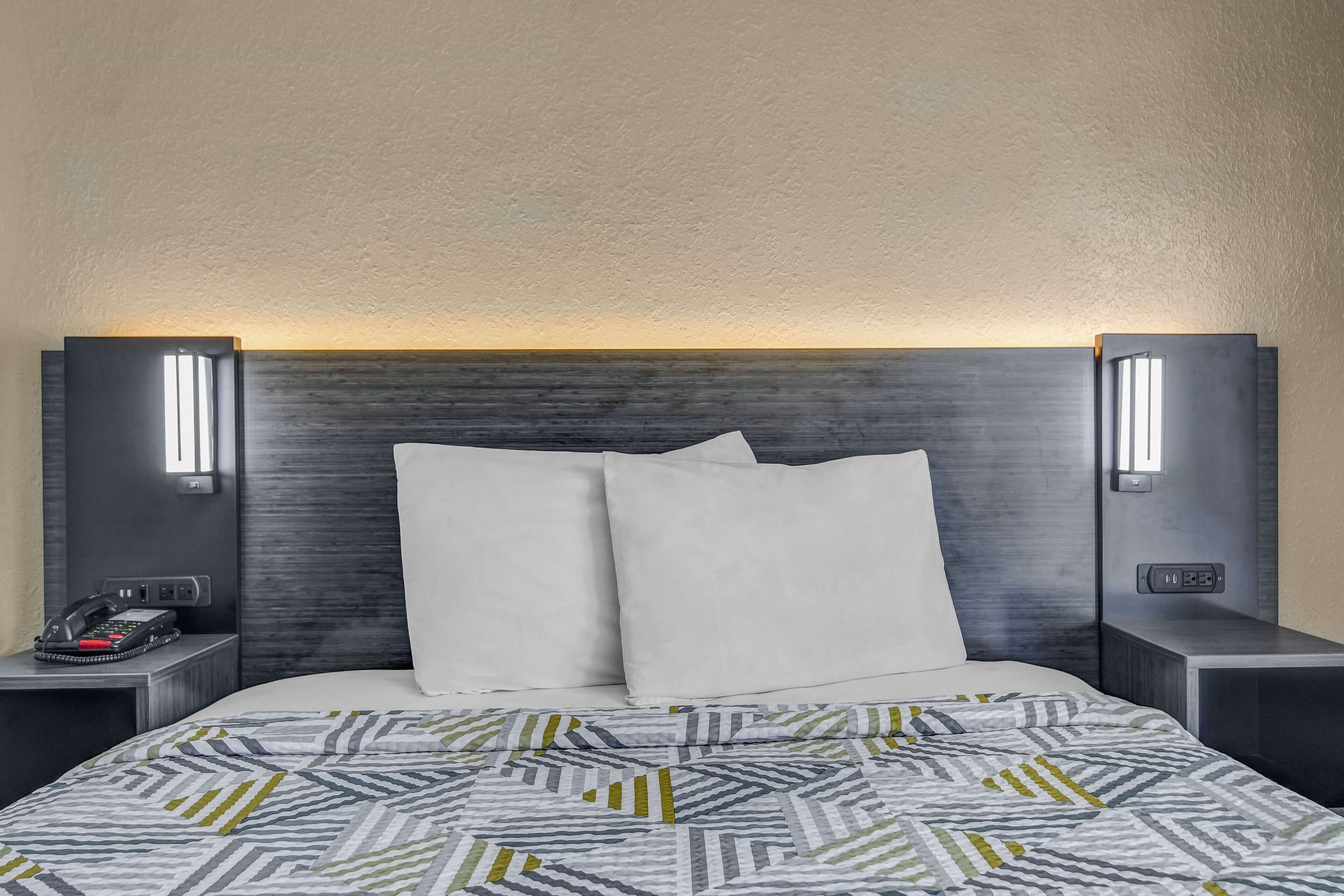 A hotel room with a bed, two bedside tables, a telephone, and wall-mounted lights.